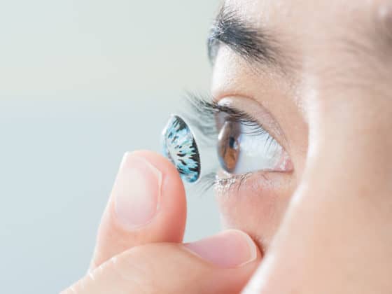 Young asian woman putting colored contact lens in her right eye, close up, selective focus at contact lens.