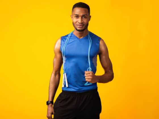 Fitness and Muscular Endurance Concept. Confident black man holding skipping rope on neck isolated over yellow studio wall,
