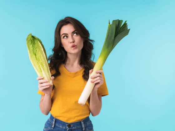 Image of thinking young beautiful woman posing isolated over blue wall background holding cabbage and leek, two nitric oxide foods.