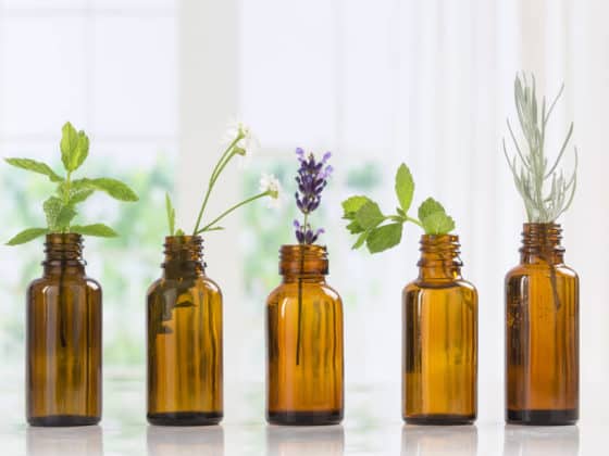 Five brown essential oil bottles with green herbs in them.